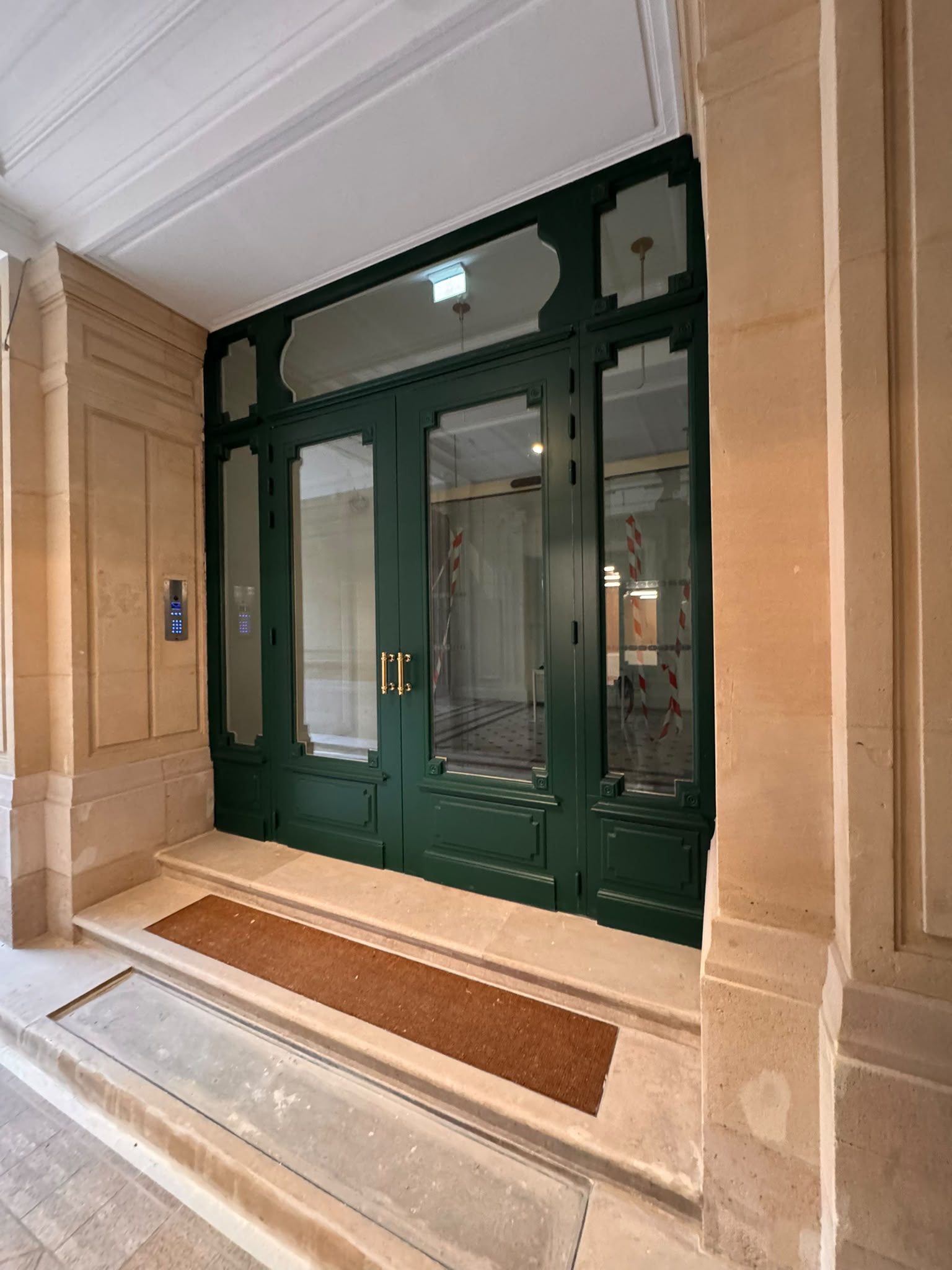 Porte d'entrée vitrée laquée verte, quincaillerie laiton, dans son encadrement pierre.